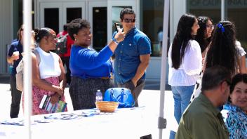 A diverse group of attendees smile, mingle, and take photos at the UC Davis Memorial Day Ceremony 2025, held outdoors in front of a campus building