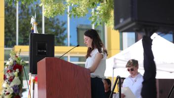 A woman addresses the audience from the podium while other speakers wait their turn, during the UC Davis Memorial Day Ceremony 2025
