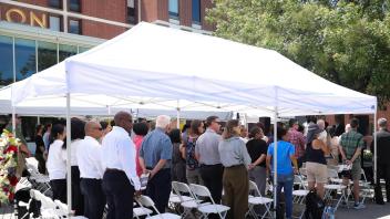 Attendees stand in respectful silence under white canopy tents during the UC Davis Memorial Day Ceremony 2025, held outside a campus building on a sunny day