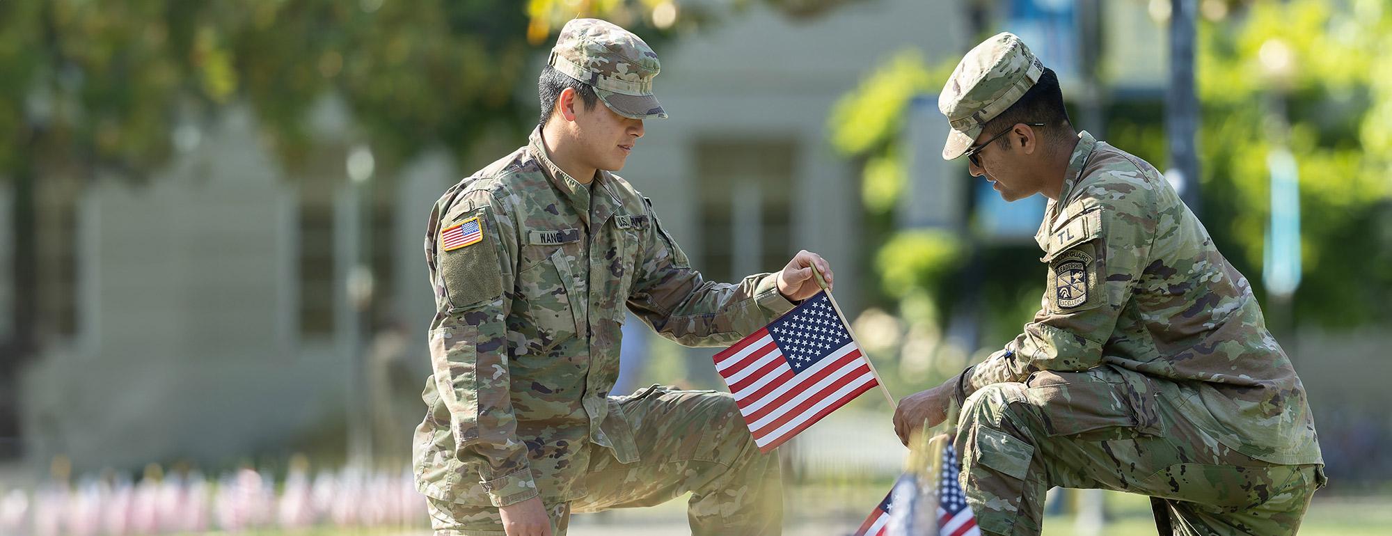 Two US Army officers in fatigues place small American flags on the lawn in front of the Memorial Union