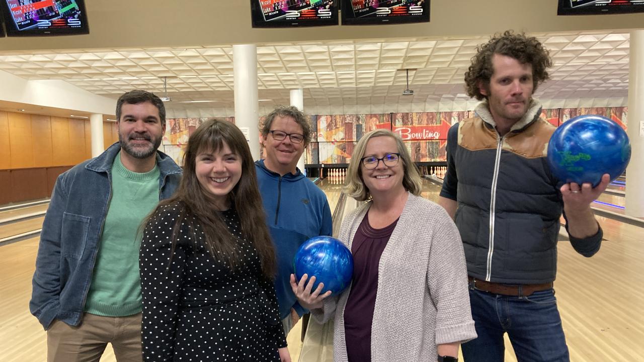 Group of 5 staff smiling in front of bowling lanes