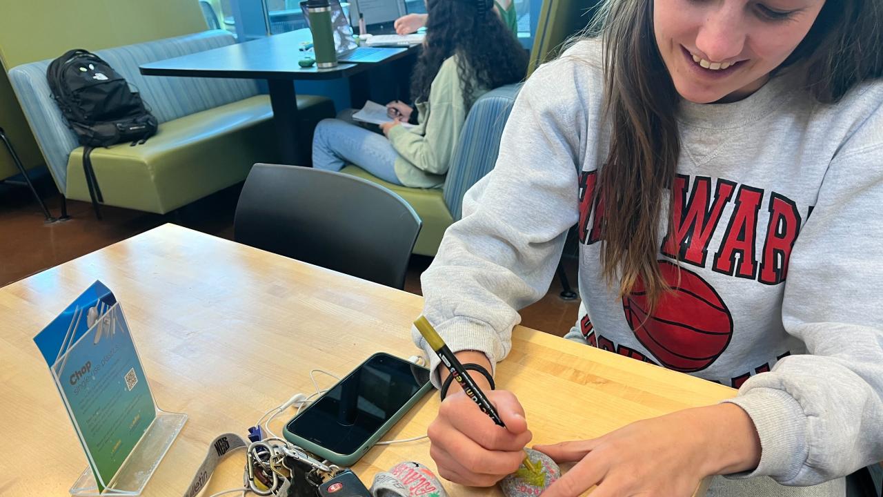 Student sitting at a table painting a rock with her keys and phone on the table
