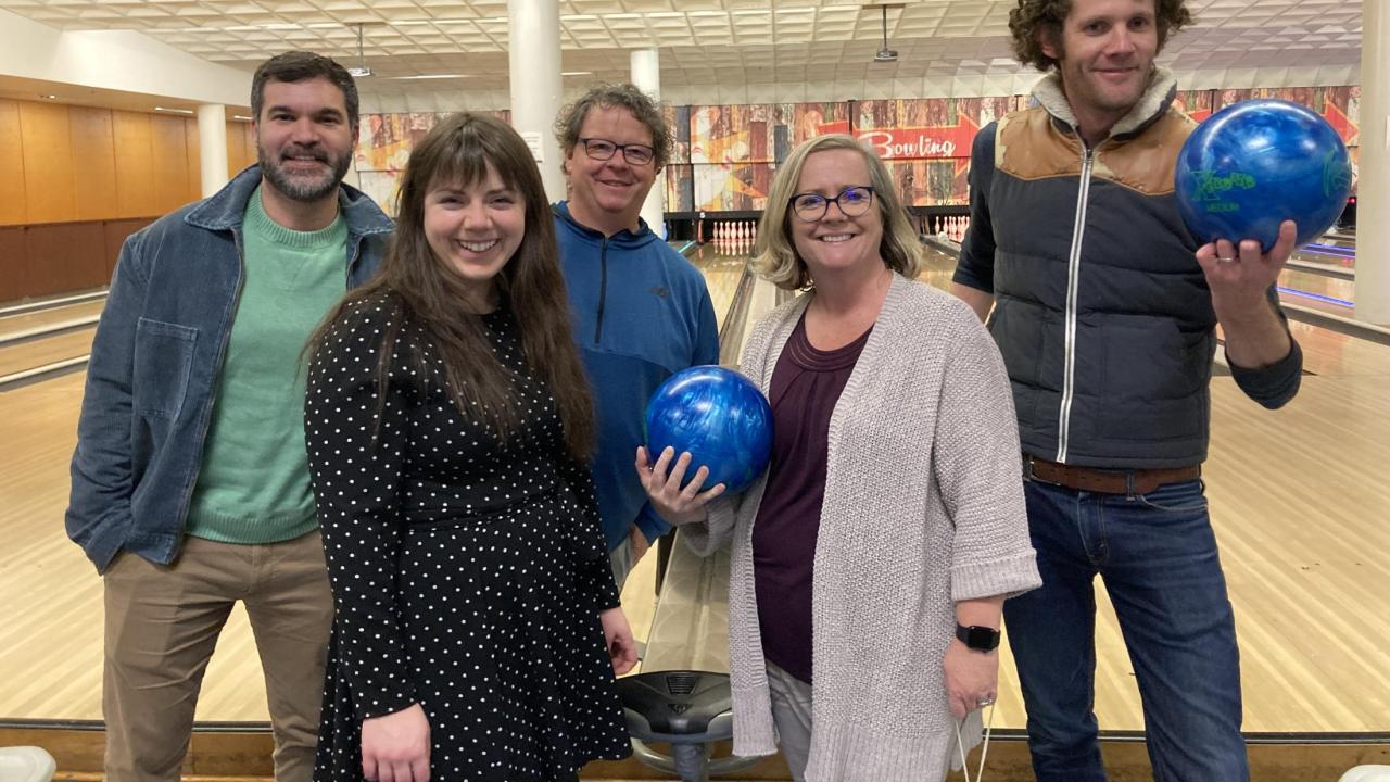 Group of 5 staff smiling in front of bowling lanes