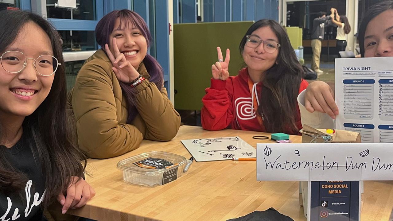 A group of students smiles and shows their trivia card