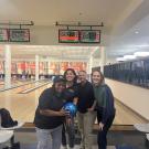 Four staff members smile and pose in front of the Games Area bowling lanes. One staff members holds up a blue bowling ball.