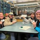 Four students sitting at a CoHo table hold up their Coffee House gift cards